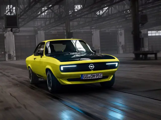 Een geel-zwarte Opel GSE-auto in retrostijl rijdt een industrieel pakhuis binnen.