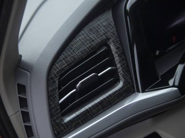 Close-up van een ventilatierooster op het dashboard van een Volkswagen Multivan met een rand met patroon en een deel van het aangrenzende touchscreen-display zichtbaar.