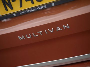 Close-up van het embleem en de kentekenplaat aan de achterkant van een roestkleurige Volkswagen Multivan, die het opvallende ontwerp laat zien.