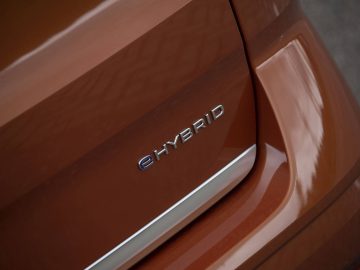 Close-up van de achterkant van een bruine Volkswagen Multivan met het "eHYBRID"-embleem, wat duidt op een hybride voertuig.