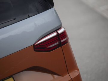 Close-up van de achterhoek van een Volkswagen Multivan, met rode achterlichtdetails tegen een oranje en grijze carrosserie.