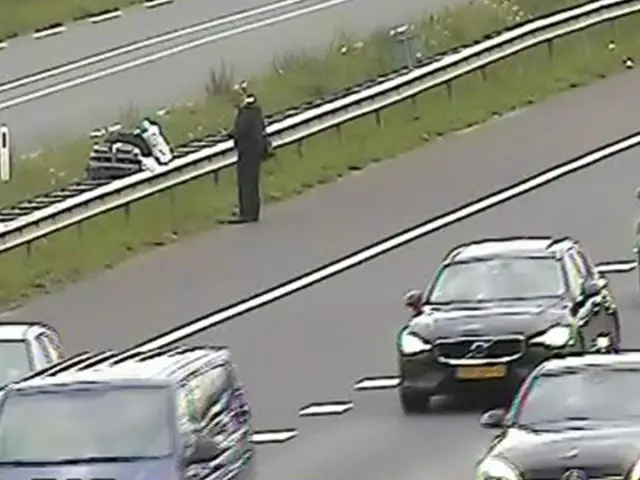 Op de berm van de A12 staat een persoon naast een motor, terwijl er meerdere auto's langsrijden op de aangrenzende rijstroken.