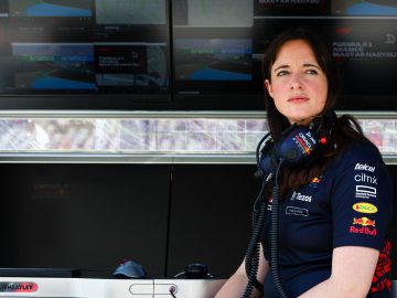Hannah Schmitz, met een headset en een Red Bull Racing-teamshirt op, zit achter een bedieningspaneel met meerdere schermen waarop racegegevens worden weergegeven.