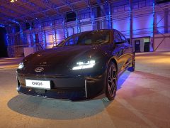 Een Hyundai IONIQ 6 sedan wordt tentoongesteld onder opvallende verlichting in industriële stijl in een binnenomgeving, wat het strakke design en de moderne techniek benadrukt.