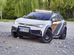 Een aangepaste Volkswagen ID. Xtreme offroad-SUV met robuuste offroad-banden en een krachtige LED-lichtbalk staat geparkeerd op een rotsachtig, bosrijk terrein.