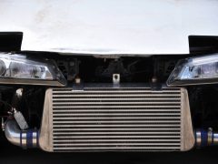 Een close-up van de voorkant van een auto waarvan de bumper is verwijderd, met de prominent aanwezige intercooler en zichtbare koplampen.