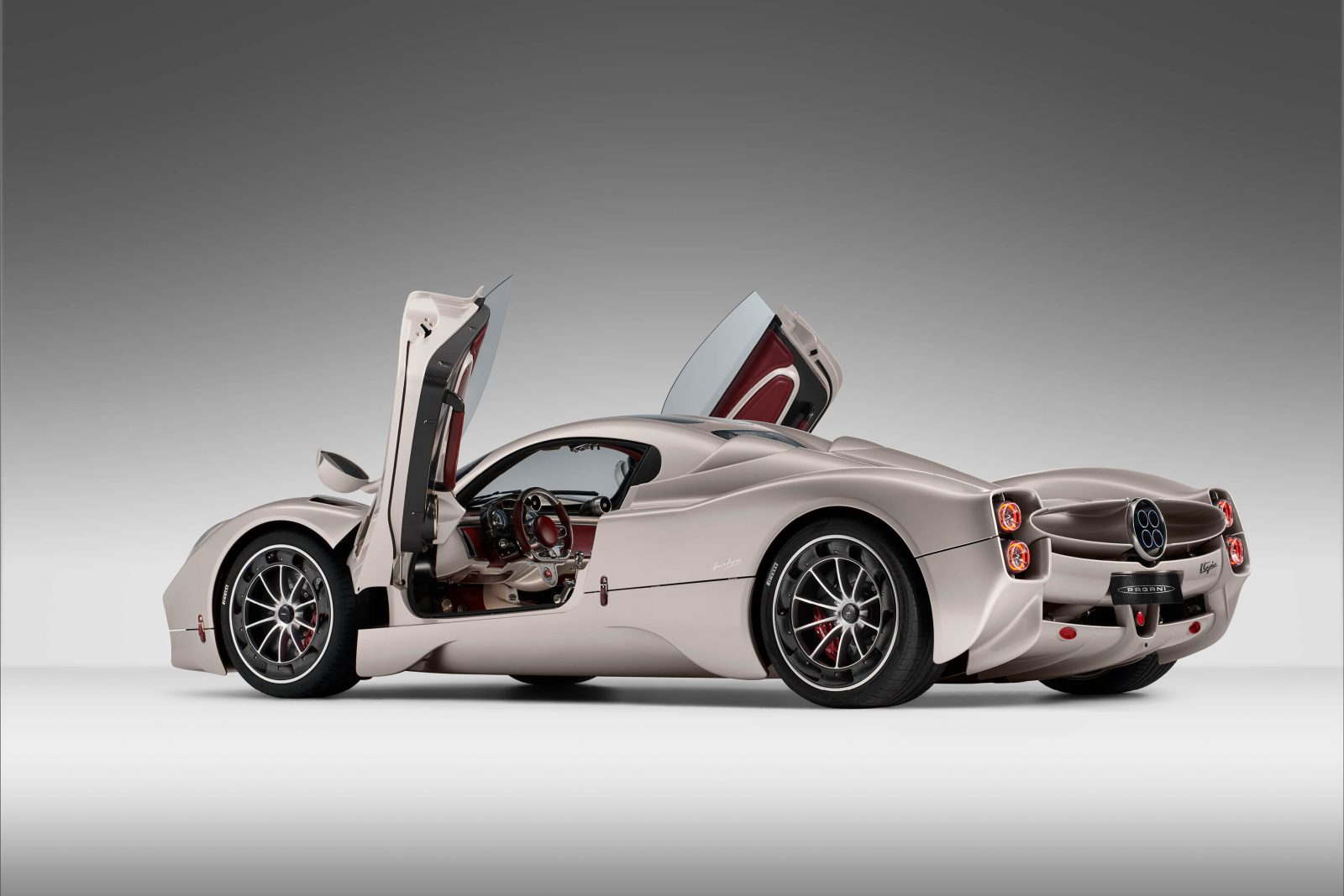 Een slanke zilveren Pagani Utopia-sportwagen met een aerodynamisch ontwerp, met open vleugeldeuren en een rood interieur. De auto wordt weergegeven tegen een effen witte achtergrond.