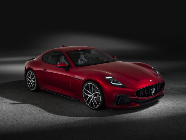 Een Maserati GranTurismo wordt verlicht tegen een donkere achtergrond, waardoor het strakke ontwerp en de lichtmetalen velgen goed tot hun recht komen.