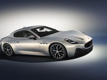 Een zilveren Maserati GranTurismo met strakke rondingen en grote wielen wordt weergegeven op een verlopende achtergrond.