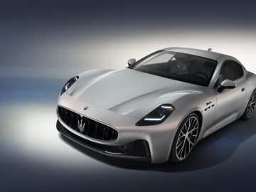 Een slanke, zilverkleurige tweedeurs Maserati GranTurismo met een modern design en een prominente grille, geparkeerd op een achtergrond met kleurverloop.