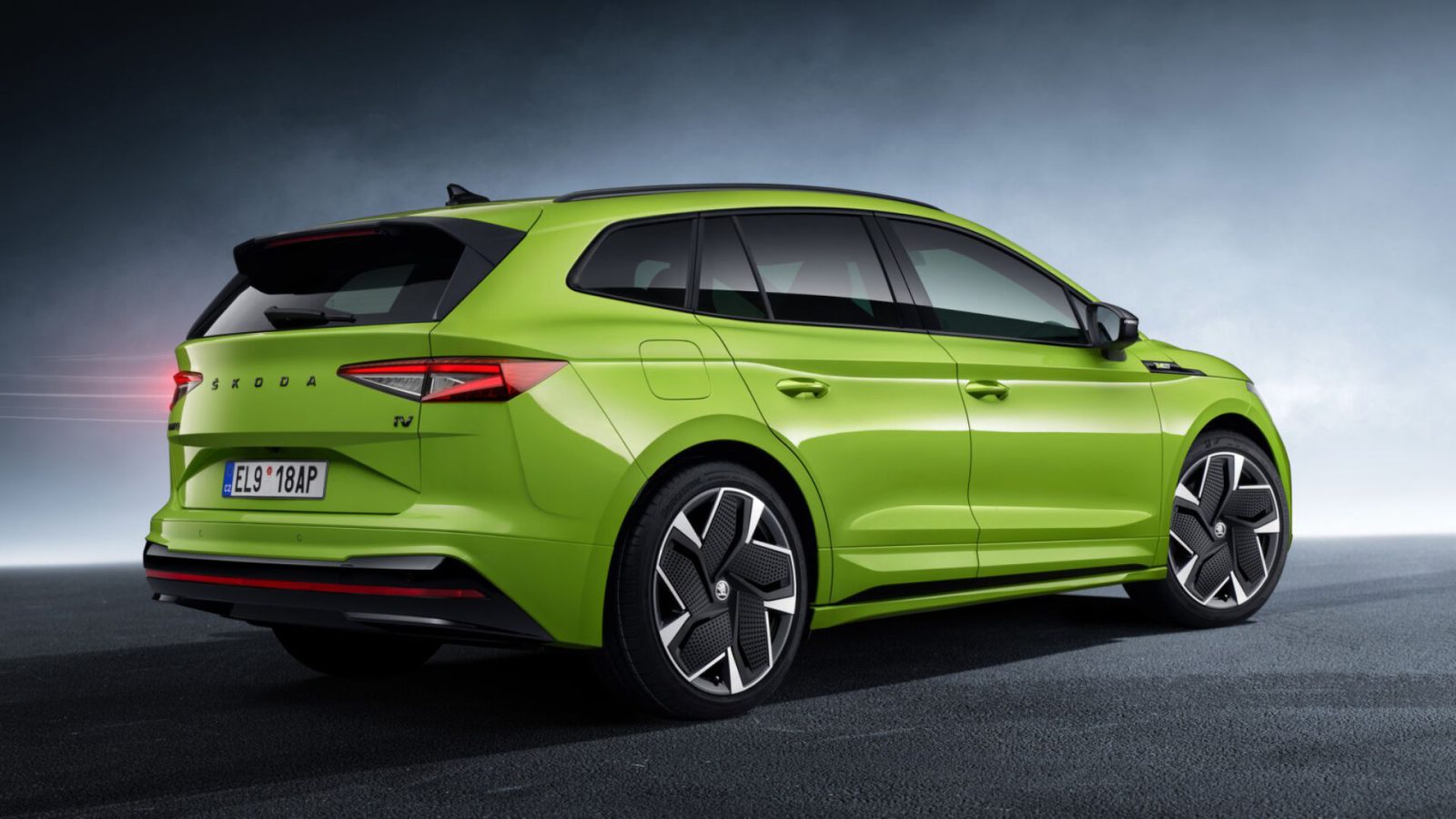 Een groene Skoda Enyaq RS staat geparkeerd op een donkere ondergrond met een mistige achtergrond. Het voertuig is linksachter bekeken en laat het strakke ontwerp en de moderne achterlichten goed zien.