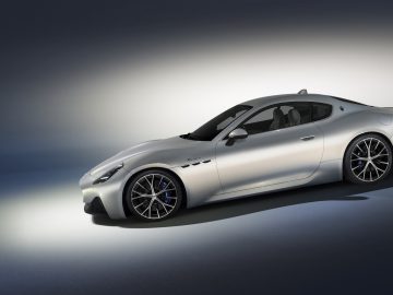 Een slanke, zilveren Maserati GranTurismo-sportwagen wordt tentoongesteld op een verlopende achtergrond, verlicht door een spotlight.