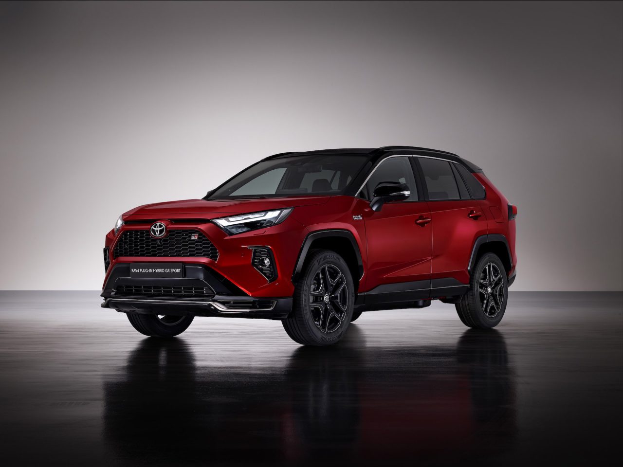 Een rood-zwarte Toyota RAV4 GR Sport plug-in hybride SUV wordt getoond in een studiosetting met een neutrale achtergrond.