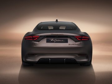 Achteraanzicht van een donkergekleurde Maserati GranTurismo-sportwagen met strak design en verlichte achterlichten, weergegeven tegen een neutrale achtergrond.