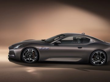 Een strakke grijze Maserati GranTurismo-sportwagen geparkeerd in een slecht verlichte studio, waar het strakke ontwerp en de stijlvolle velgen goed tot hun recht komen.