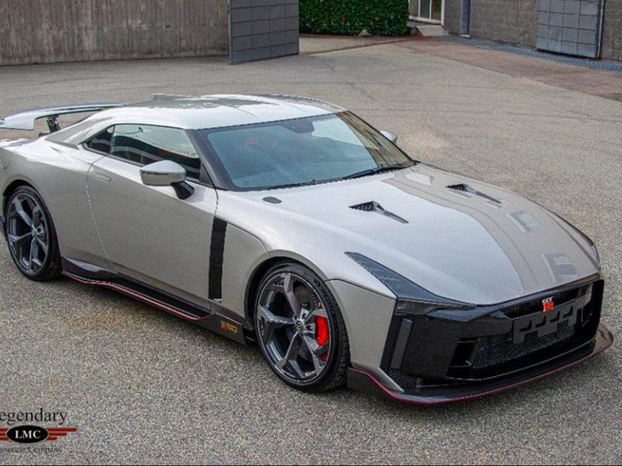 Een zilveren high-performance Nissan GT-R met zwarte accenten en rode remklauwen, geparkeerd op een verharde ondergrond. Hij beschikt over een strak, aerodynamisch ontwerp met zichtbare merk- en modelinsignes op de grille.