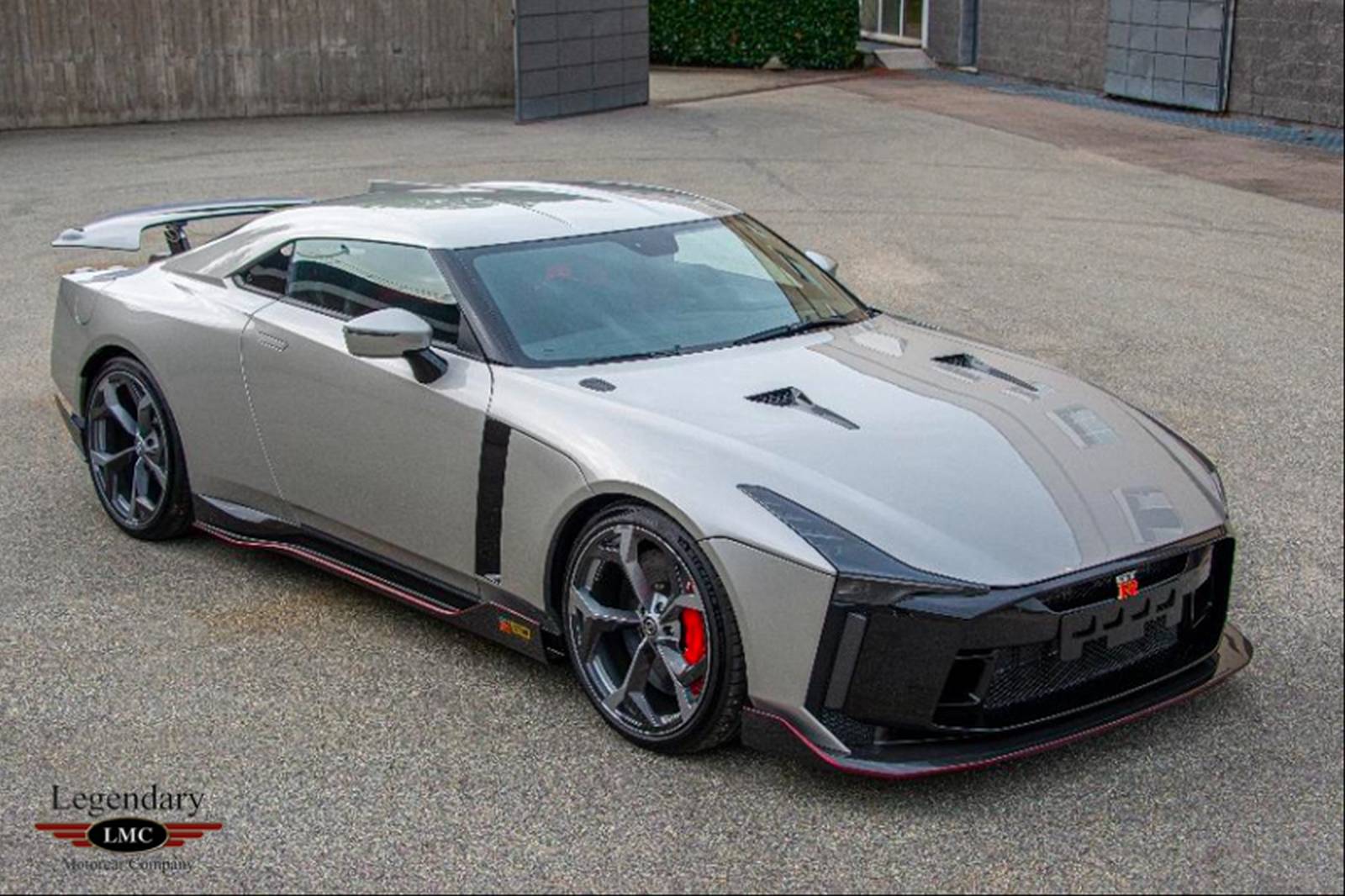 Een zilveren high-performance Nissan GT-R met zwarte accenten en rode remklauwen, geparkeerd op een verharde ondergrond. Hij beschikt over een strak, aerodynamisch ontwerp met zichtbare merk- en modelinsignes op de grille.