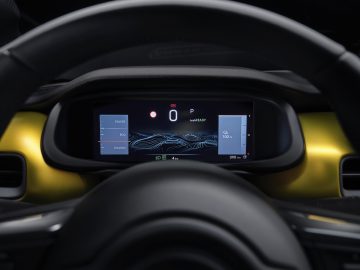 Close-up van het digitale dashboard van een Jeep Avenger met een snelheidsmeter, vermogens- en eco-instellingen, samen met het batterijniveau van 100%. Het stuur is gedeeltelijk zichtbaar.