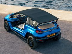 Een blauwe compacte Coastrunner EV met een zwart softtopdak staat aan het water geparkeerd op een betonnen ondergrond. Het elektrische voertuig heeft een open ontwerp met twee stoelen en een zichtbaar stuur.