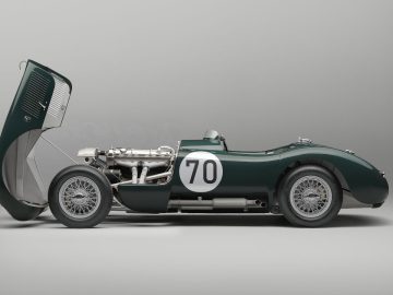 Zijaanzicht van een vintage Jaguar C-Type racewagen met het nummer 70 op de deur geschilderd. De motorkap van de auto is open, waardoor de motor zichtbaar wordt. Het voertuig is donkergroen en heeft spaakwielen.