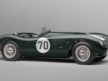 Een vintage groene Jaguar C-Type raceauto met het nummer 70 op de zijkant, met een strak, aerodynamisch ontwerp en zilverdraadspaakwielen, weergegeven tegen een effen grijze achtergrond.