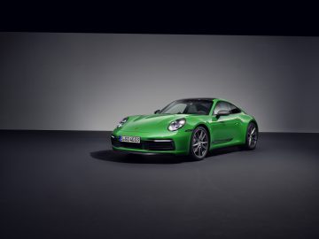 Een groene Porsche 911 Carrera T-sportwagen staat geparkeerd op een donkere ondergrond tegen een grijze achtergrond, iets naar links gericht.