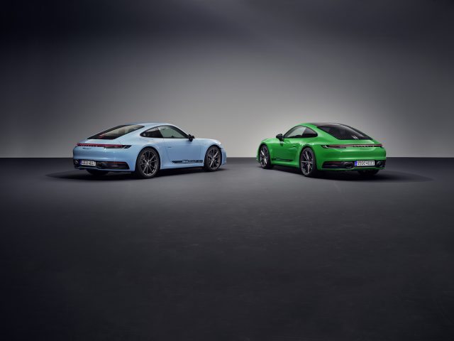 In een slecht verlichte showroom worden twee sportwagens tentoongesteld. De ene Porsche 911 Carrera T is lichtblauw met zwarte accenten en de andere is heldergroen, beide schuin naar elkaar toe gericht.