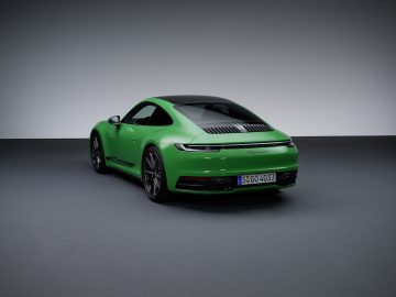 In een minimalistische studiosetting wordt een groene Porsche 911 Carrera T met een strak design en donker getinte ruiten tentoongesteld. De auto heeft een zwart dak en een zichtbaar kenteken met de tekst "S-GO 4033.