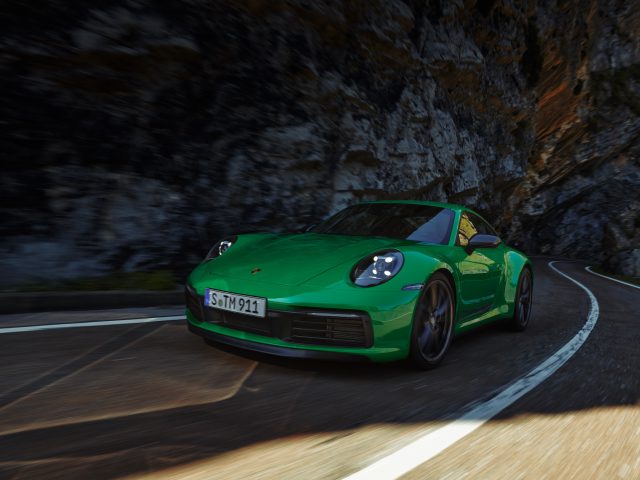 Een groene Porsche 911 Carrera T rijdt over een kronkelende bergweg, met majestueuze rotswanden op de achtergrond.