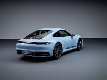 Binnen staat een lichtblauwe Porsche 911 Carrera T met een strak design geparkeerd, gezien vanaf de achterkant en linkerkant. Op het kenteken staat "S-GO 4043".