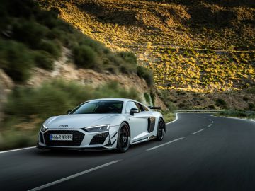 Een witte Audi R8 Coupé V10 GT RWD rijdt overdag over een bochtige weg door een bergachtig landschap.