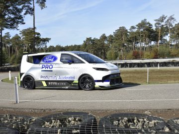 Een elektrische bestelwagen van Ford E-Transit die over een racecircuit met een bosrijke omgeving navigeert. Het busje is voorzien van branding en aerodynamische aanpassingen.