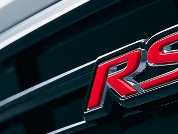 Close-up van een rood en chroom "RS"-badge op een zwarte Honda Jazz-grille.