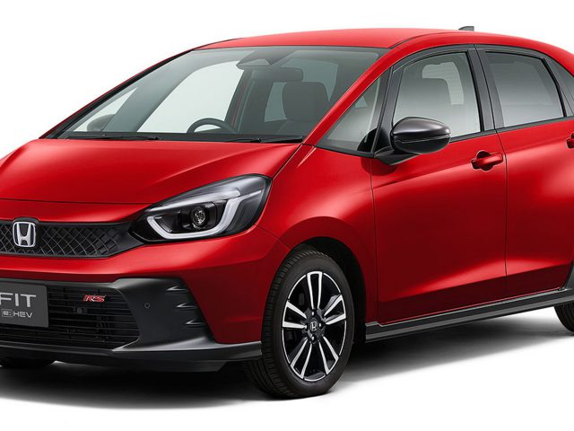 Een rode compacte Honda Fit e:HEV-auto, vergelijkbaar met de Honda Jazz RS, staat geparkeerd en toont de voor- en zijkant met het merklogo en de modelnaam zichtbaar op de grille.