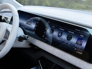 Close-up van het moderne autodashboard van de Mitsubishi XFC Concept met een groot digitaal display met navigatie, mediabediening en verschillende meters. Het stuur en enkele ventilatieopeningen zijn zichtbaar.