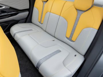 De afbeelding toont de achterbank van een Mitsubishi XFC Concept-auto met grijze en gele bekleding, inclusief hoofdsteunen, en is gepositioneerd naast een lege grijze autovloer.