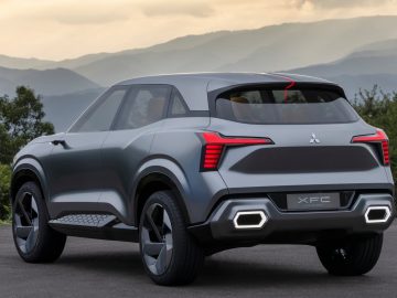 Een grijze Mitsubishi XFC Concept SUV staat geparkeerd op een weg met bergen en een bewolkte lucht op de achtergrond. De auto heeft scherpe hoeken, LED-achterlichten en grote wielen.