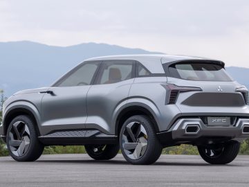 Een zilverkleurige futuristische SUV met strakke lijnen en een modern design staat geparkeerd op een weg met bergen op de achtergrond. Op de achterkant is de modelnaam "Mitsubishi XFC Concept" zichtbaar.