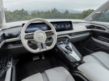 Modern auto-interieur met een digitaal dashboard, een strak stuur met het Mitsubishi-logo en een futuristische middenconsole. Ook beschikt deze Mitsubishi XFC Concept over een voorruit die uitzicht biedt op groen op de achtergrond.