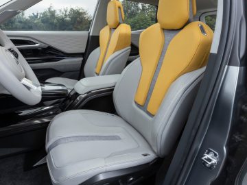 Een modern auto-interieur met witte en gele lederen stoelen, een wit stuur en een middenconsole die doet denken aan de Mitsubishi XFC Concept. De achtergrond toont een zicht op bomen door de ramen.