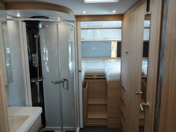 Het interieur van een moderne camper bestaat uit een compacte slaapkamer met een bed, een badkamer met een douchehoek, houten kasten en overal opberglades.