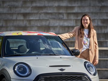 Een persoon in een lichtbruin pak staat naast een witte MINI Cooper met een kleurrijke MINI Rooftop.