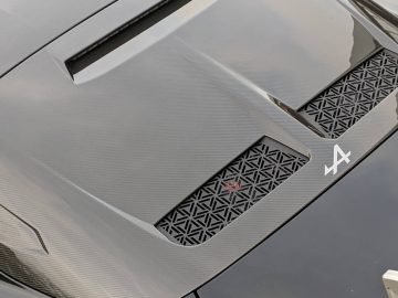 Close-up van de achterkant van een slanke, donkergekleurde sportwagen met een ingewikkeld ontwerp van de ventilatieopeningen en een opvallend Alpine A110-logo.