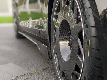 Close-up van het achterwiel en de band van een zwarte Alpine A110-auto. De band is een Michelin Pilot Sport Cup 2 met zichtbaar loopvlak en het lichtmetalen velg is voorzien van een koolstofvezelontwerp.