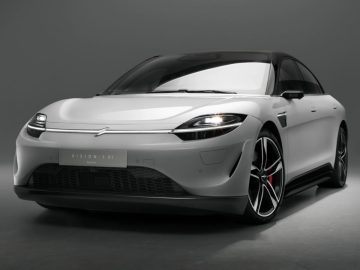 Een moderne witte elektrische sedan van Honda met strak design, zwarte accenten en rode remklauwen wordt getoond in een studiosetting. De auto, die beschikt over door Sony geïntegreerde technologie, heeft een aerodynamisch profiel aan de voorkant en opvallende koplampen.