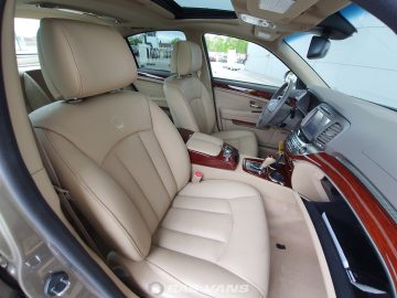 Interieur van de Ssangyong Chairman CW700 met beige lederen stoelen, een houten bekleding, een schuifdak en een middenconsole met verschillende bedieningselementen.