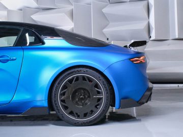 Zijaanzicht van een blauwe Alpine A110 R in een moderne, geometrische setting, met nadruk op de achterkant, het achterlicht en het grote zwarte lichtmetalen velg.