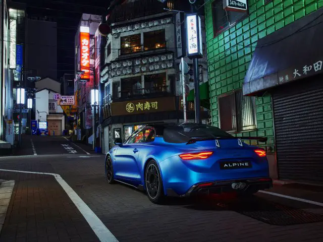 In een smal straatje staat 's nachts een Alpine A110 R geparkeerd, omringd door gebouwen met verlichte Japanse borden.