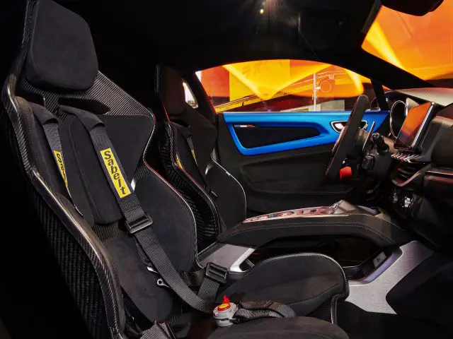 Interieur van een Alpine A110 R-sportwagen met twee racestoelen met 'Sabelt'-harnassen, een strak dashboard en een levendig blauw deurpaneel.