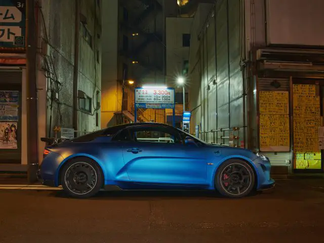 Een Alpine A110 R staat 's nachts geparkeerd in een smalle stadsstraat, verlicht door omringende straatverlichting en bouwborden.